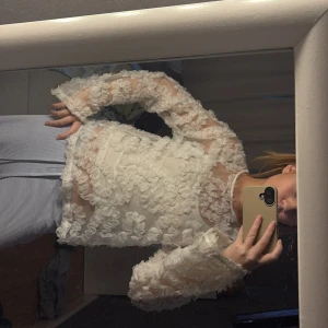 Vit blommig blus - Säljer en vacker vit blus med blommigt mönster och långa ärmar. Blusen har en transparent design med 3D-blommor som ger en romantisk känsla. Perfekt för att lyfta vilken outfit som helst.
