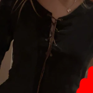 Svart tröja med snörning - Snygg svart tröja med snörning framtill och unika mönstrade detaljer på ärmarna. Perfekt för en stilren look med en twist. Passar bra till både jeans och kjol.