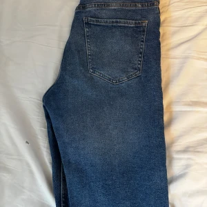 Blå jeans från Bershka - Snygga blå jeans från Bershka med klassisk femficksdesign och knappgylf. Jeansen har en rak passform och är perfekta för en avslappnad stil. De har en lätt tvättad look som ger en trendig touch.