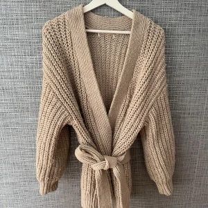 Beige stickad kofta med bälte - En beige stickad knutkofta, materialet är väldigt tjockt och värmande.