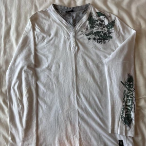 Alternativ långärmad t-shirt från Okay - Vit långärmad tröja från Okay med tryck i grönt och svart. Tröjan har en knappdetalj vid halsen och ett tryck på ärmen och bröstet. Jättebra skick! Den är i storlek XL men skulle säga att det är storlek M