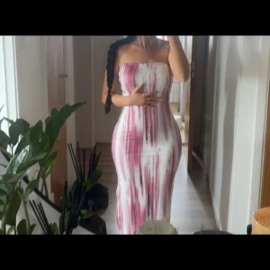 Axelbandslös klänning med rosa mönster - Snygg axelbandslös klänning med ett unikt rosa och vitt mönster. Klänningen är lång och har en tight passform