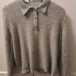 Grå stickad tröja med krage - Säljer en mysig grå stickad tröja med krage och tre dekorativa knappar framtill. Perfekt för kyliga dagar och ger en stilren look. Passar bra till både jeans och kjol. Orginal pris 359kr. Går att diskutera pris som vanligt.