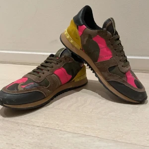 Valentino Rockrunner  - Snygga Valentino Rockrunner sneakers med ett unikt camouflagemönster i rosa, grönt och brunt. Skick 8/10. Skorna har en kombination av mocka och skinn, med en iögonfallande gul häl. Perfekta för att ge din outfit en färgklick. Skriv vid minsta lill fundering👌🏼