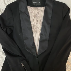 Svart kavaj från Stockh LM - Elegant svart kavaj från Stockh LM med en stilren design. Kavajen har en klassisk krage och är helfodrad med ett ljust innerfoder. Perfekt för en formell look.