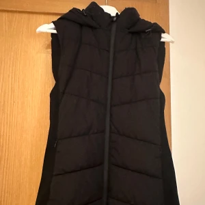 Svart dunväst med huva - Snygg svart dunväst med dragkedja och huva. Perfekt för kyliga dagar när du vill hålla värmen utan att bära en jacka. Västen har en quiltad design som ger en stilren look. Från Zara - slutsåld - Zara warrior väst säljs pga inte kommer till användning  🖤