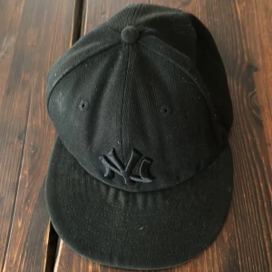 Svart keps från New Era - Snygg svart keps från New Era med broderad logga framtill. Kepsen har en klassisk design med platt skärm och är perfekt för en casual look. Tillverkad i bomull för en bekväm passform.