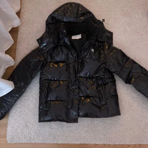 Svart pufferjacka från Calvin Klein - Säljer min eftertraktade jacka. Den kommer inte till användning. Den är i storlek M men passar xs/s jag själv har s och xs. Fint skick och använd fåtal gånger💕Slutsåld på nätet. Köptes för 3999kr.#Calvinklein#glansig#vinterjacka