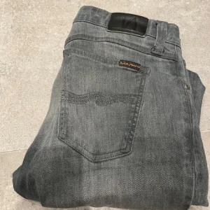 Grå Nudie Jeans - Säljer ett par grå jeans från Nudie Jeans i storlek 30/32. De sitter väldigt najs och är mycket sköna. De har en snygg tvättad look och är gråa