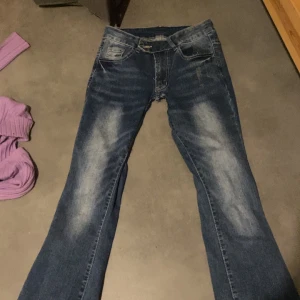 Blå jeans med slitningar - Säljer ett par blå jeans med snygga slitningar. De har en klassisk femficksdesign och knappgylf. Perfekta för en avslappnad stil. Har sytt ner de själv .