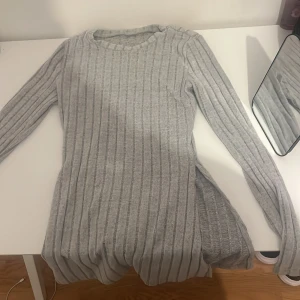 Grå ribbad stickad tröja och byxor - Säljer ett set med en grå ribbad stickad tröja och matchande byxor. Tröjan har långa ärmar och en rund halsringning. Byxorna är långa och har en elastisk midja för bekväm passform. Perfekt för en mysig dag hemma!