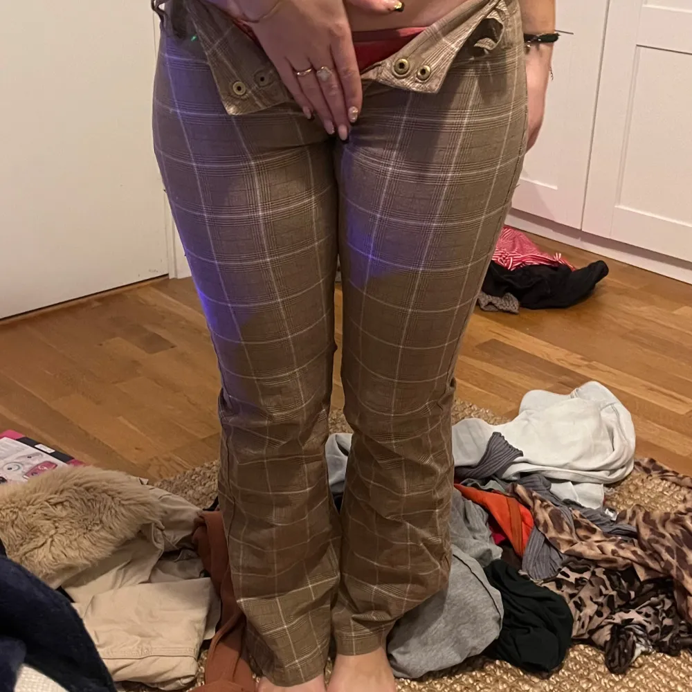 Säljer ett par bruna rutiga byxor med låg midja och bootcut-stil. Byxorna har knappar och dragkedja framtill. Perfekta för en trendig look! Sydda lågmidjade med ett litet hål vid skrevet men inget som syns passar någon upp till 155. Farkut & Housut.