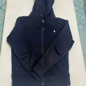 Mörkblå hoodie från Ralph Lauren - Snygg mörkblå hoodie från Ralph Lauren med dragkedja och klassisk logga på bröstet. Perfekt för en avslappnad stil. Priset går att diskuteras. Köp den inte direkt kontakta mig först. Tack.