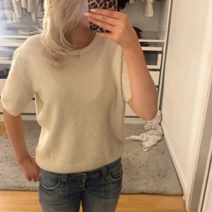 Beige stickad tröja - Säljer en stilren beige stickad tröja med korta ärmar. Perfekt för en avslappnad look. Tröjan har en rund halsringning och är gjord i ett mjukt material.