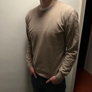 Beige tröja från Oscar Jacobson - Säljer en stilren beige tröja från Oscar Jacobson. Tröjan har en rund hals och är tillverkad i Italien (100% merinoull). Perfekt för en elegant och avslappnad look. Storlek L men sitter mer som en M.