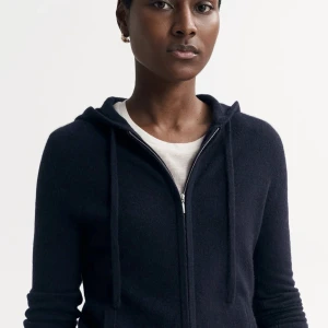 Mörkblå hoodie från Soft Goat - Snygg och bekväm mörkblå hoodie från Soft Goat i kashmir. Tröjan har dragkedja framtill och en praktisk huva med knytband. Perfekt för kyliga dagar.