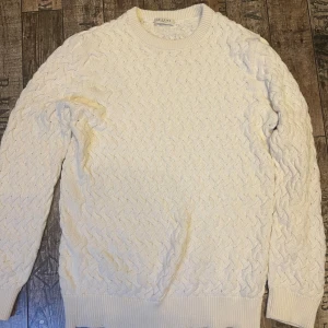 Vit/beige stickad tröja - Säljer en stilren vit stickad tröja från Selected Homme. Tröjan har ett snyggt kabelstickat mönster och långa ärmar. Perfekt för kyligare dagar.