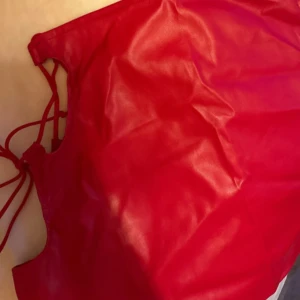 Röd minikjol från PrettyLittleThing - Snygg röd minikjol i lack från PrettyLittleThing med snörning/ öppen sida. Perfekt för en halloween fest eller andra finare tillställningar. Den slutar strax under rumpan. Säljer då den inte kommer till användning. Prisklapp kvar, helt oanvänd.