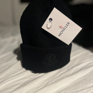 Moncler mössa - En helt ny, läcker Moncler-mössa lite annorlunda mot den klassiska hatten, i All Black😋♠️, med denna mössa kan du inte gå fel på stan med One size fits all, super bra kvalitet📸, väska och tak ingår, äntligen lägg ett bud eller fråga🫡