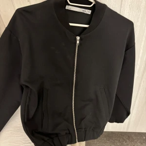 Svart bomberjacka från 157 - Snygg svart bomberjacka från 157 med dragkedja framtill. Jackan har en klassisk design med ribbade muddar vid ärmslut och nederkant. Perfekt för en stilren look.