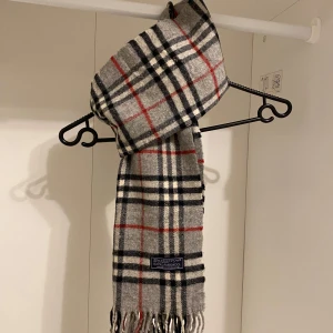 Burberry - Säljer nu denna Snygga halsduk från Burberry i färgen grå. Tillverkad i mjukt lammull med klassiskt fransad kant. Perfekt för att hålla dig varm och stilren under kyliga dagar. Hör av er vid funderingar☺️
