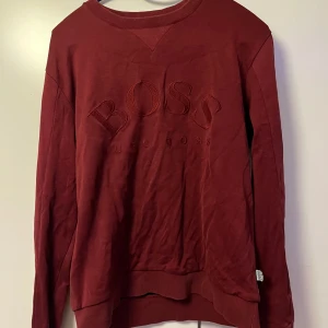 Vinröd tröja från Hugo Boss - Snygg vinröd tröja från Hugo Boss med broderad logga på framsidan. Nåt speciellt tyg på baksidan