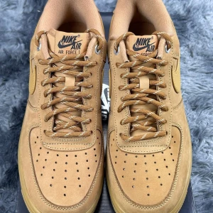 Bruna Nike Air Force 1 - Snygga bruna Nike Air Force 1 sneakers i mocka med klassisk design. Skorna har perforerade detaljer för ventilation och en robust sula för komfort. Perfekta för en stilren look.