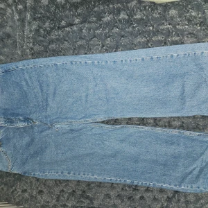 Blå jeans från NA-KD - Säljer ett par klassiska blå jeans från NA-KD i storlek 42. De har en rak passform och är tillverkade i denim med traditionella fem fickor och knappgylf. Perfekta för en avslappnad stil.