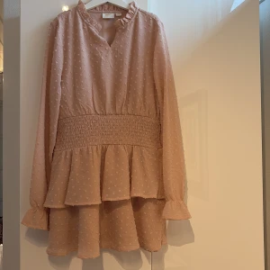 Rosa klänning från Gina Tricot - Söt rosa klänning från Gina Tricot med volangdetaljer och smock i midjan. Klänningen har långa ärmar och ett diskret prickigt mönster. Mycket bra skick och finns inte i sotumentet längre.