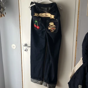 Mörkblå jeans med broderade detaljer - (Intressekoll) Unika mörkblå jeans med coola broderade detaljer som körsbär och text på bakfickorna. Jeansen har en loose passform , hög midja och är uppvikta vid bensluten. Midjemått 76 och innerbenslängd 81 🍒