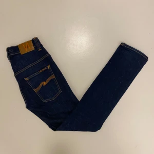  Nudie Jeans ”Tape Ted” - Snygga mörkblå jeans från Nudie Jeans med klassisk femficksdesign och kontrastsömmar. (Använda max 3 gånger) Jeansen är i modellen Tape Ted vilket är en slim passform och är tillverkade i högkvalitativt denim. Perfekta för en stilren look.