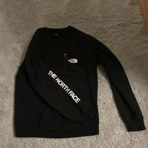 Tröja The North Face - Säljer en svart tröja från The North Face med logotyp på bröstet och ärmen. Tröjan har långa ärmar och en klassisk passform. Perfekt för en stilren och bekväm look.