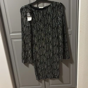 Svart glittrig klänning från NLY TREND - Snygg svart klänning från NLY TREND med glittrigt mönster. Den har en tight passform och långa ärmar, perfekt för en kväll ute. 