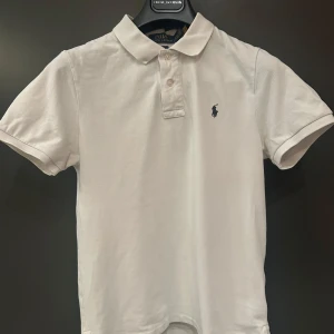 Vit pikétröja från Ralph Lauren strl 170 - Vit pikétröja från Ralph Lauren i Slim Fit. Använd sparsamt och därmed i ett mycket fint befintligt skick. Inga fläckar eller defekter förekommer därför. Hör av dig vid funderingar. Perfekt till sommaren! 