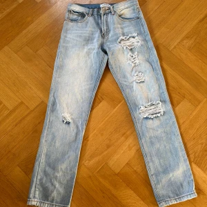 Lågmidjade Ljusa jeans med slitningar från Glamorous - Säljer ett par ljusa lågmidjade jeans från Glamorous i storlek XS. De har coola slitningar på framsidan och en klassisk femficksdesign. Perfekta för en avslappnad stil med en touch av edge. Rak passform