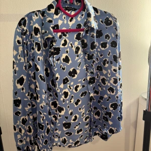 Blå leopardmönstrad blus - Snygg blå blus med leopardmönster i svart och vitt. Blusen har långa ärmar och en klassisk krage. Perfekt för att ge din outfit en trendig touch.