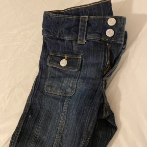 Snygga mörkblå flared jeans / stl EUR 140 - Snygga mörkblå jeans med två framträdande knappar och dragkedja. De har en klassisk design med fickor och kontrastsömmar. Perfekta för en avslappnad stil.