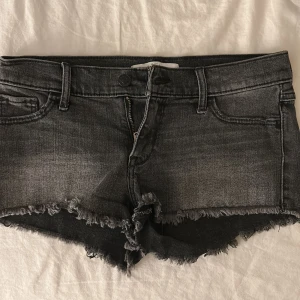 Svarta jeansshorts från Abercrombie & Fitch - Snygga svarta / grå jeansshorts från Abercrombie & Fitch med fransiga kanter och klassisk femficksdesign. Perfekta för en avslappnad stil. De har en knapp och dragkedja framtill. Köpta från Plick men aldrig använda av mig.