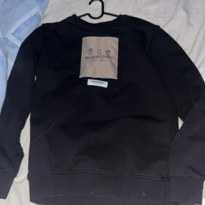 Svart sweatshirt från Burberry - Snygg svart sweatshirt från Burberry med en beige patch på bröstet och Burberry-logga. Perfekt för en stilren look.