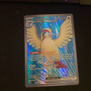 Pidgeot EX Pokémonkort full art - Säljer ett holografiskt Pidgeot EX Pokémonkort med förmågan 'Quick Search' och attacken 'Blustery Wind'. Kortet har en glansig yta med blå och regnbågsfärgade detaljer. Perfekt för samlare eller spelare som vill förstärka sin kortlek.