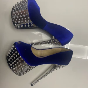 Blå pumps med nitar - Snygga blå pumps med hög klack och spetsig tå. Skorna har en unik design med silverfärgade nitar på klacken och sulan, vilket ger dem en edgy look. Perfekta för att sticka ut på festen!