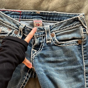 true religon jeans - Snygga blå jeans med unika broderade detaljer och knappar på bakfickorna. De har en lågmidjad passform och en straight leg tyvärr åt skinny hållet som ger en cool look. Perfekta för dig som vill ha något annorlunda i garderoben. köpte 1200 nya Använd en gång till skolan