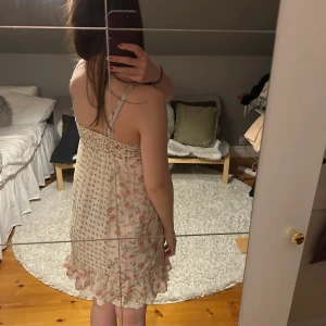 Blommig sommarklänning med volang - Söt blommig klänning i ljusa färger med volangdetaljer längst ner. Klänningen är ärmlös och har smala axelband, perfekt för varma sommardagar. Den har en avslappnad passform och knappar framtill som ger en extra touch. Klänningen är i strl 152 och jag är ca 160 cm