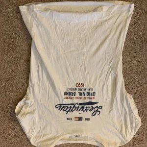 Vit t-shirt från Lexington - Säljer en vit t-shirt från Lexington med tryck på framsidan. T-shirten är kortärmad och tillverkad i bomull. Perfekt för en avslappnad stil.