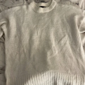 Vit stickad tröja - Säljer en mysig vit stickad tröja med rund hals och långa ärmar. Perfekt för kyliga dagar och enkel att matcha med olika outfits. Tröjan har en klassisk design med ribbstickade muddar vid ärmslut och nederkant.