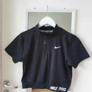 Kortärmad träningstopp från NIKE - Säljer en svart  kortärmad topp från Nike med dragkedja framtill och Dri-FIT teknologi. Perfekt för träning med en sportig look och bekväm passform. Nike-logga på bröstet och texten 'NIKE PRO' vid nederkanten. 🏋️‍♀️