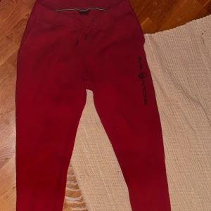Röda mjukisbyxor från Sail Racing - Snygga röda mjukisbyxor från Sail Racing med snörning i midjan och tryckt logga på benet. Perfekta för en avslappnad stil. De har en bekväm passform och är gjorda i mjukt material. Size L men sitter mer som S (längden är L, bredden är typ S)