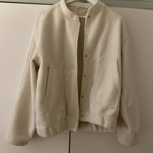 Bomberjacka - Säljer en mysig vit bomberjacka med tryckknappar framtill. Jackan har långa ärmar och två stora fickor på framsidan. Perfekt för kyliga dagar. Oversized. 