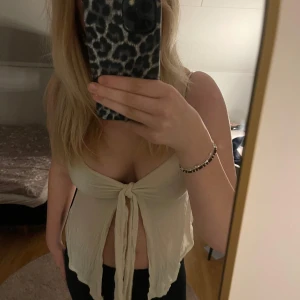 Beige knytblus - Säljer en stilren beige blus med knyt framtill. Den är ärmlös och har en djup v-ringning, perfekt för varmare dagar. Passar bra till både jeans och kjol.