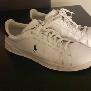 Vita sneakers från Ralph Lauren strl 45 - Snygga vita sneakers från Ralph Lauren med klassisk Polo-logga på sidan. Skorna har svarta detaljer vid hälen och snörning framtill. Perfekta för en stilren look.